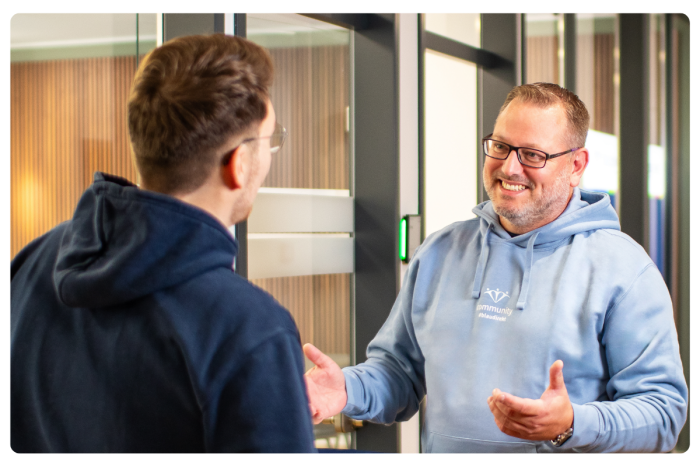 2 Männer unterhalten sich. Einer trägt einen hellblauen Hoodie mit der Aufschrift "Community".